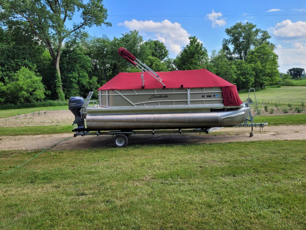 Custom red pontoon boat cover installed on trailer showcasing marine upholstery and boat cover services in Michigan